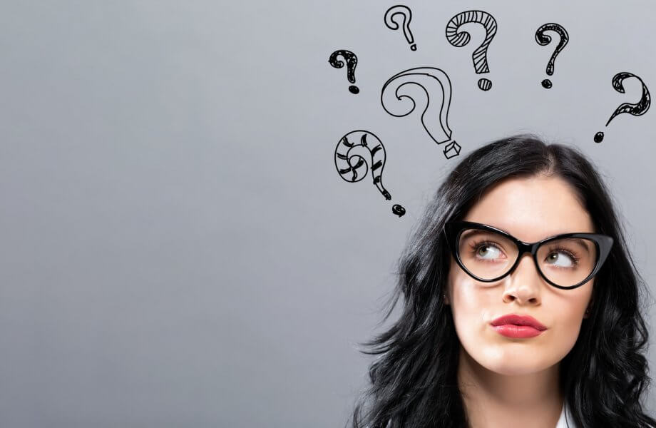 Photograph of a woman with long black hair & glasses looking up. There are hand drawn question marks over her head.