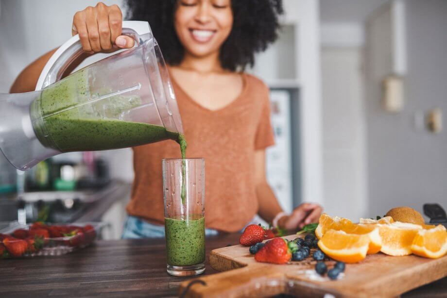 woman pours smoothy in fruit-filled kitchen