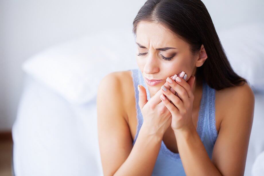 woman holds jaw and grimaces in pain